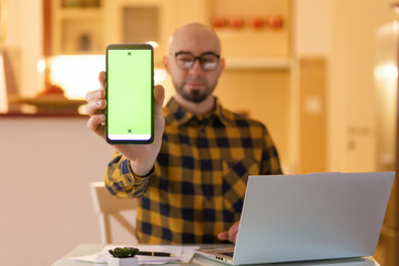 Freelance and online communication. Portrait of smiling Caucasian bald bearded young man shows green screen of cellphone. Concept of remote work and freelance