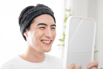 Very user-friendly beauty image of an Asian man looking in the mirror with a hair band up