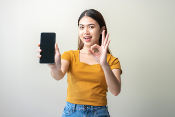 Naklejka premium Portrait of positive expression asian young woman, female show finger ok sign, holding mobile phone in hand showing application on blank smartphone screen, isolated on white background, copy space.