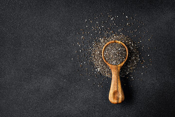 top view of chia seeds in round wooden scoop on black background