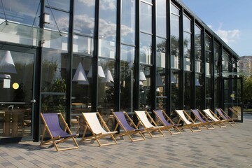 Empty wooden deck chairs near modern cafe in a public park. Outdoor summer terrace area for...