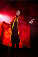 Witch woman in red cloak with skull on black background and light in night. Female warrior in the Dark