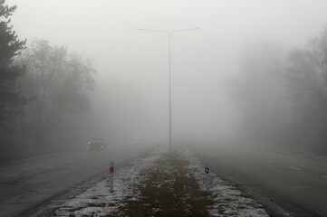 Car traveling on the foggy road with headlights or headlamps on. Low visibility - Dangerous driving of cars in winter in bad weather.
