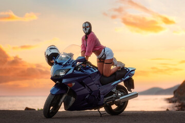 Sexy woman in a balaclava with skull poses on a tourist motorcycle. Beautiful golden sunset in the background. The concept of moto travel and motorcycle world day - obrazy, fototapety, plakaty