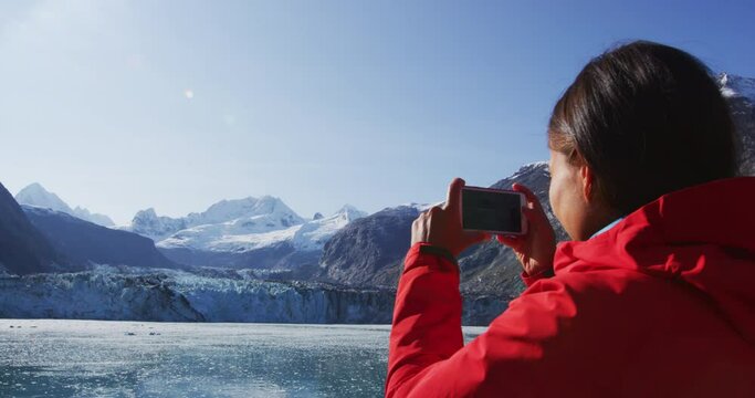 Alaska travel woman taking photo on phone of Glacier Bay Alaska. Cruise ship passenger in Glacier Bay National Park, USA. Woman on travel in Inside Passage enjoying view of Johns Hopkins Glacier