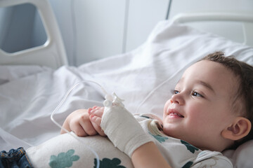 little boy in hospital lying in bed with an intravenous line in his hand smiling