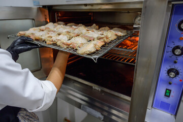 Chef in white coat prepares fresh chicken in big oven. Baked chicken menu. View from outside of...
