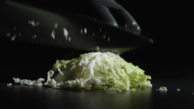 A man-cook in black gloves cuts green cabbage with a knife