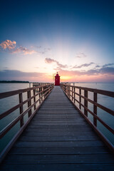 Fototapeta na wymiar Leuchtturm mit Steg und Sonne zum Sonnenaufgang.