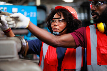Black Woman worker wearing safety goggles control lathe machine to drill components. Metal lathe industrial manufacturing factory. Team work