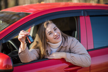 Happy young woman sits in her new car and shows the keys, the girl passed the car driving test