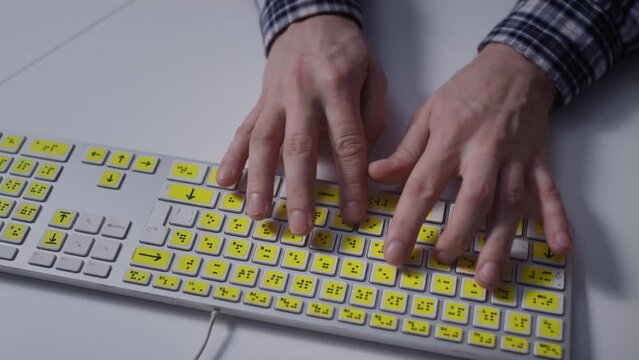 Close-up: A man uses a keyboard with braille.A blind man is typing words on the buttons with her hands. Technological device for visually impaired people. Tactilely touches bumps on the keys