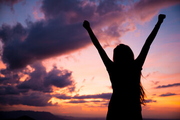woman gesturing success - silhouette over evening sky with clouds and vibrant colors of a sunset