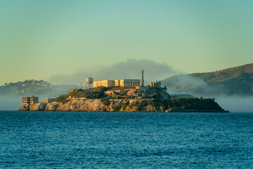 Alcatraz island with buildings in golden sunset or sunrise and foggy background with dark blue...
