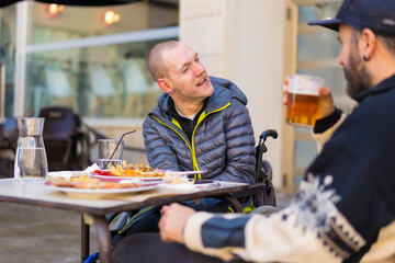 A disabled person eating and smiling with a friend having fun, terrace of a restaurant