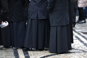 Ksiądz katolicki w birecie na procesji trzech króli. Czarna postać.