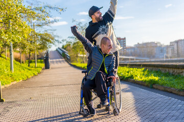 Fototapeta na wymiar Disabled person in wheelchair with friend overjoyed, smiling, enjoying with arms up, vistoria, enjoying life