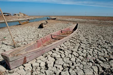 Foto auf Acrylglas A traditional Marsh Arab canoe known as a Mashoof abandoned on the dry cracked earth of the southern marshes of Iraq during a hash summer drought.  © John Wreford 