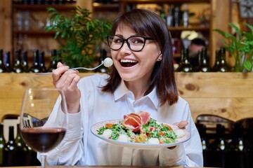 Middle-aged happy woman eating salad in restaurant, joyful face close-up
