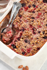 breakfast casserole idea - oven berry baked oatmeal in a white porcelain baking form on a marble board, top view