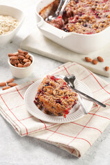 breakfast casserole idea - a piece of oven berry baked oatmeal with almonds, walnuts and coconut flakes on a white porcelain dessert plate on a checkered kitchen napkin