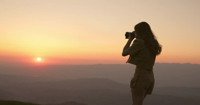 A young creative woman climbed a mountain to take her best photo at sunset, to fight procrastination and clearing thoughts on one with herself. Freelance photographer at work in an amazing location.