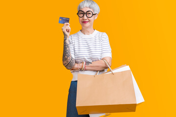 Asian happy senior female woman tattoo holds colourful shop packages standing on yellow background...