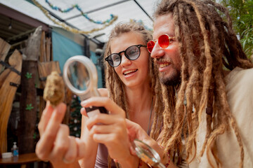 Hippie style couple examines under a magnifying glass the joints and buds of medical marijuana