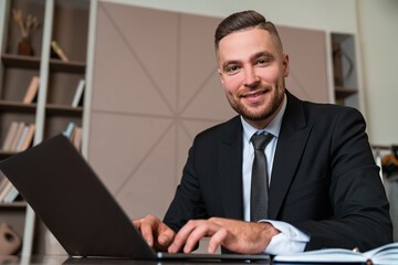 Businessman typing in laptop, happy portrait in office room