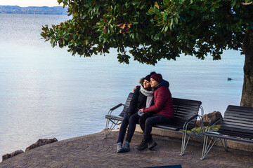 A couple sitting on a bench under a tree with a lake behind them