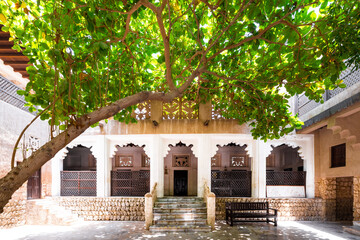 Ancient traditional house in old Dubai, with a porch lined with marble columns providing shade and an oak tree in the foreground