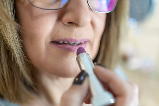 Close-up of an older white woman painting her lips in front of the mirror.