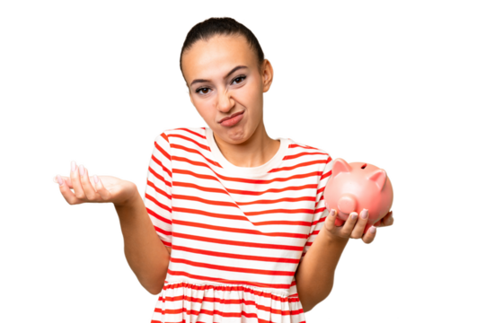 Young Arab woman holding a piggybank over isolated background making doubts gesture while lifting the shoulders