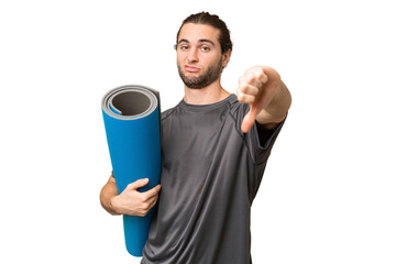 Young sport man going to yoga classes while holding a mat over isolated background showing thumb...