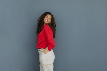 Young woman in red shirt standing against grey wall