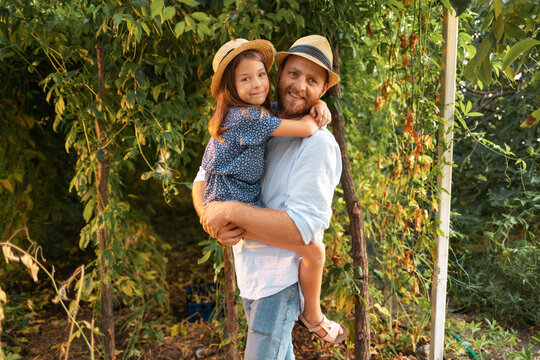 Family's vacation. Happy bearded father in a straw hat hugs his daughter. Garden in the background. The concept of Father's Day and happy childhood