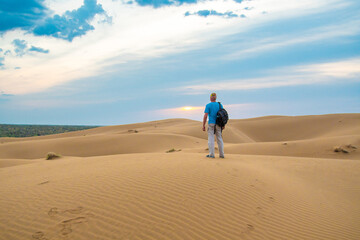 Fototapeta na wymiar One man stands on a sand dune in the Kyzylkum desert at sunrise.
