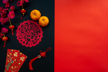 Chinese lunar new year decoration over red and black background. Flat lay concept with tangerine, red envelope, plum and festive decoration. Translation for word on decoration mean “blessing”.
