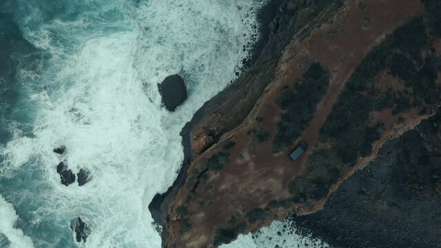 Epic And Majestic Aerial Top Down View On Small 4x4 Camper Van Drive On Offroad Gravel Path Near Steep Ocean Cliff. Exploring Rugged Coast Of Portugal In Overlanding Vehicle