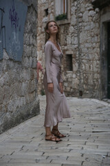 Fototapeta na wymiar Fashionable tourist woman in silk beige dress in the streets of Old town of Sibenik, Croatia