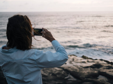 woman taking a picture of the sunset over the ocean