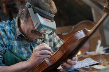 Violin maker painting violin using magnification