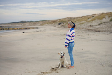 Middle-aged brunette woman on the empty beach with her labrador retriever dog