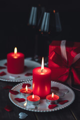 Saint Valentine's Day celebration. Red burning candles, hearts, gift box, postcard on dark wooden background. Happy holiday . Table decor for festive dinner, romantic atmosphere