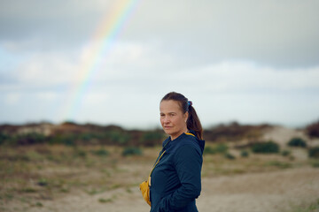 Middle-aged woman looking thoughtful at the camera with a rainbow in the background, concept for future outlook
