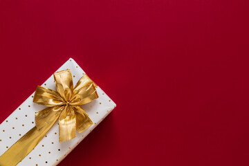 White gift box with golden ribbon and bow on a burgundy background. Top view. Copy space.