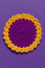 Crochet purple coaster with yellow border on a purple background. Top view.