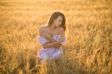 Fototapeta na wymiar portrait of a happy young girl in a dress in a wheat field at sunset, the concept of peace and unity with nature