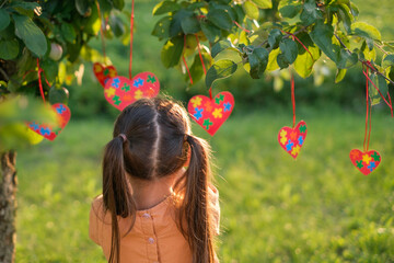 A girl decorates tree branches with hearts with colorful puzzles inside on the day of autism...