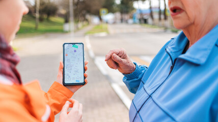 A woman holds a smartphone with an online map and shows the way to an elderly woman with her hand. Close up. Concept of lost at city